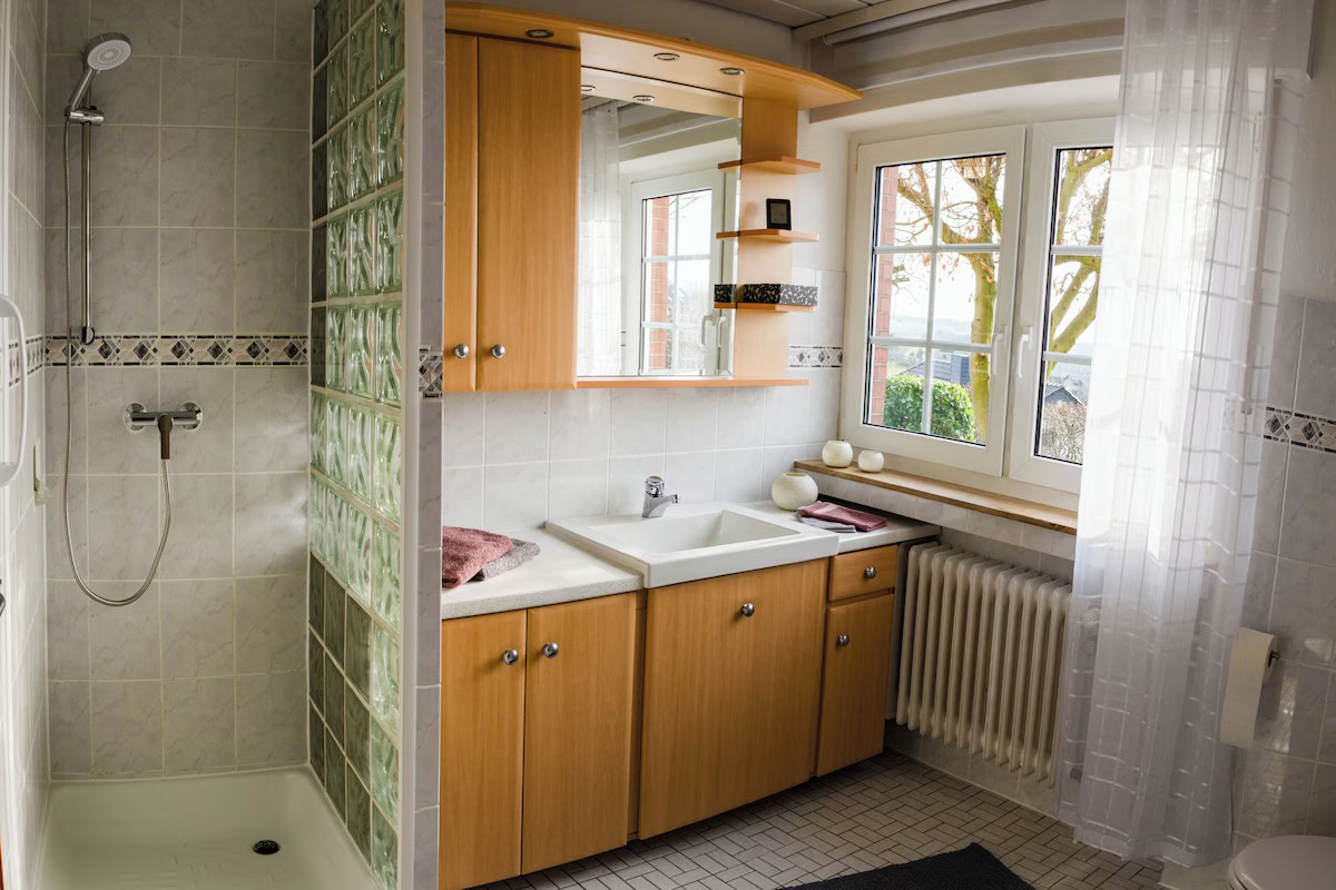 Badezimmer mit ebenerdiger Dusche hinter Glasbausteinen, Waschbecken und Fenster ins Grüne