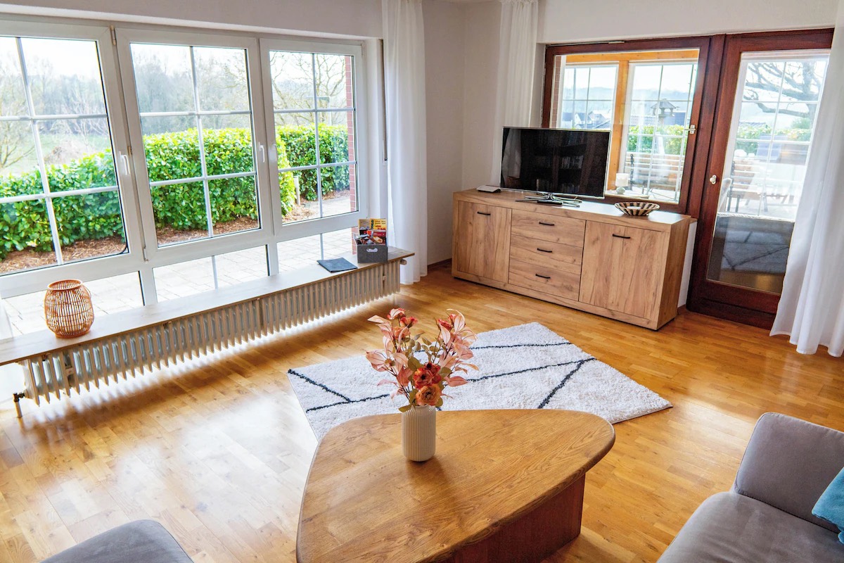 Heller Wohnraum mit Parkettboden, breiter Fensterfront ins Grüne, Sideboard und Fernseher